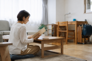 子どもの学習机があるリビングで資料を確認する女性