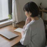 窓辺の机でノートと書類を前に予算を考える女性