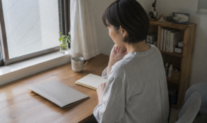 窓辺の机でノートと書類を前に予算を考える女性