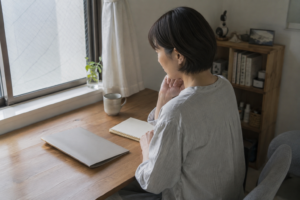 窓辺の机でノートと書類を前に予算を考える女性