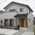 明るい曇り空の下に建つ一般的な二階建て住宅