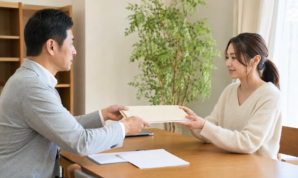 住宅相談の机で担当者から資料を受け取る女性