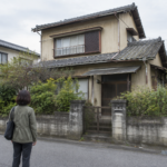 道路から古い戸建て住宅の外観を確認する女性の後ろ姿