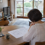 住み慣れた家のダイニングで間取り図を確認する女性の後ろ姿